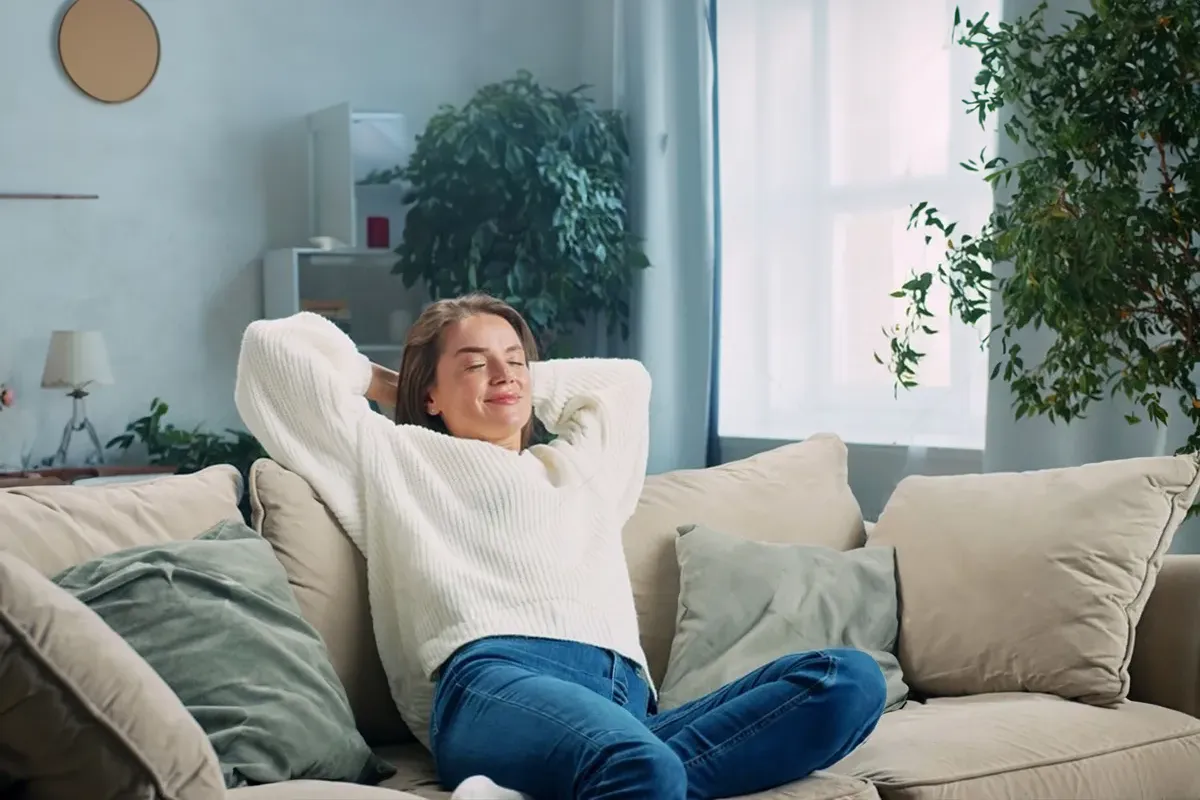 Eine weibliche Person liegt entspannt mit den armen hinterm Kopf verschränkt auf einer hellen Couch