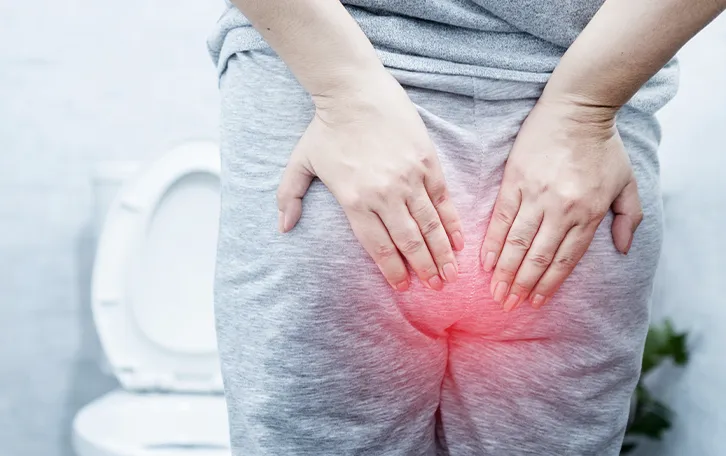 Eine weibliche Person in Jogginanzug vor einer Toilette stehend, mit schemenhaften roten Afterbereich und Händen davor